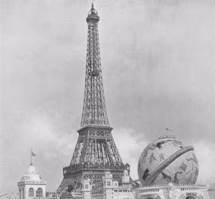 Image en noir et blanc de l'exposition Universelle  montrant une maquette de la Tour Eiffel avec des bâtiments et un globe terrestre artistique en arrière-plan. Exposition où la manufacture Pillivuyt a reçu plusieurs médailles.
