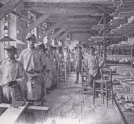 Photo historique des ateliers porcelainiers Pillivuyt. Groupe d'ouvriers dans l'usine Pillivuyt  avec des étagères remplies de moules en porcelaine.