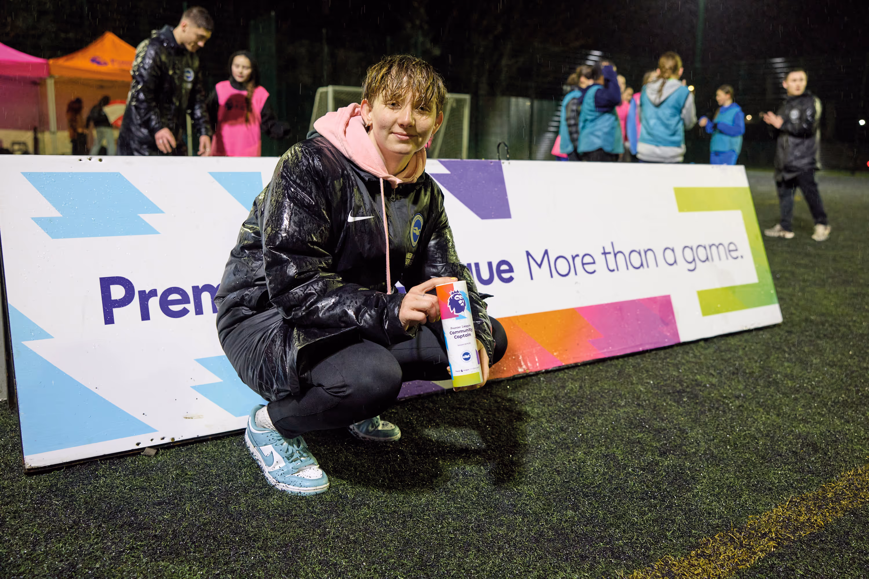 Brighton's Community Captain Jaime holds her trophy in front of a Premier League More Than a Game board.