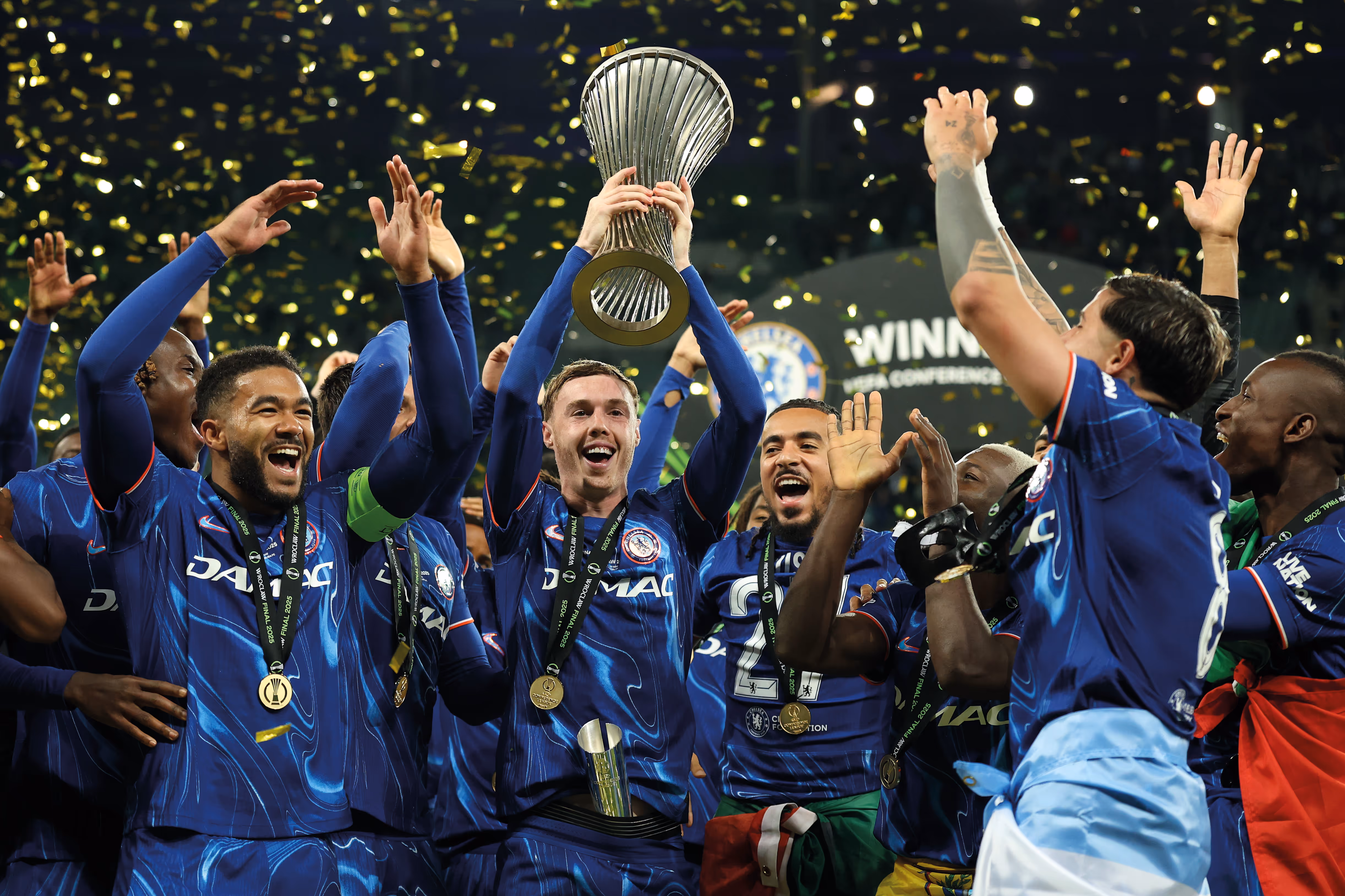 Chelsea players including Cole Palmer and Reece James hold the UEFA Conference League trophy and smile.