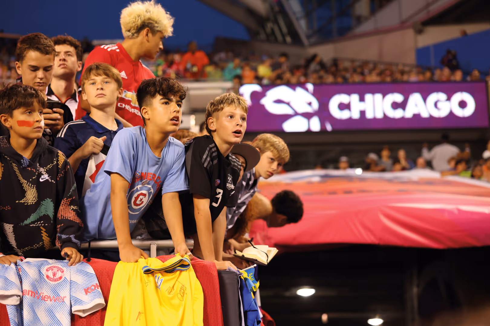 Young fans lean forwards while watching the Premier League Summer Series. A sign behind them says 'Chicago'.
