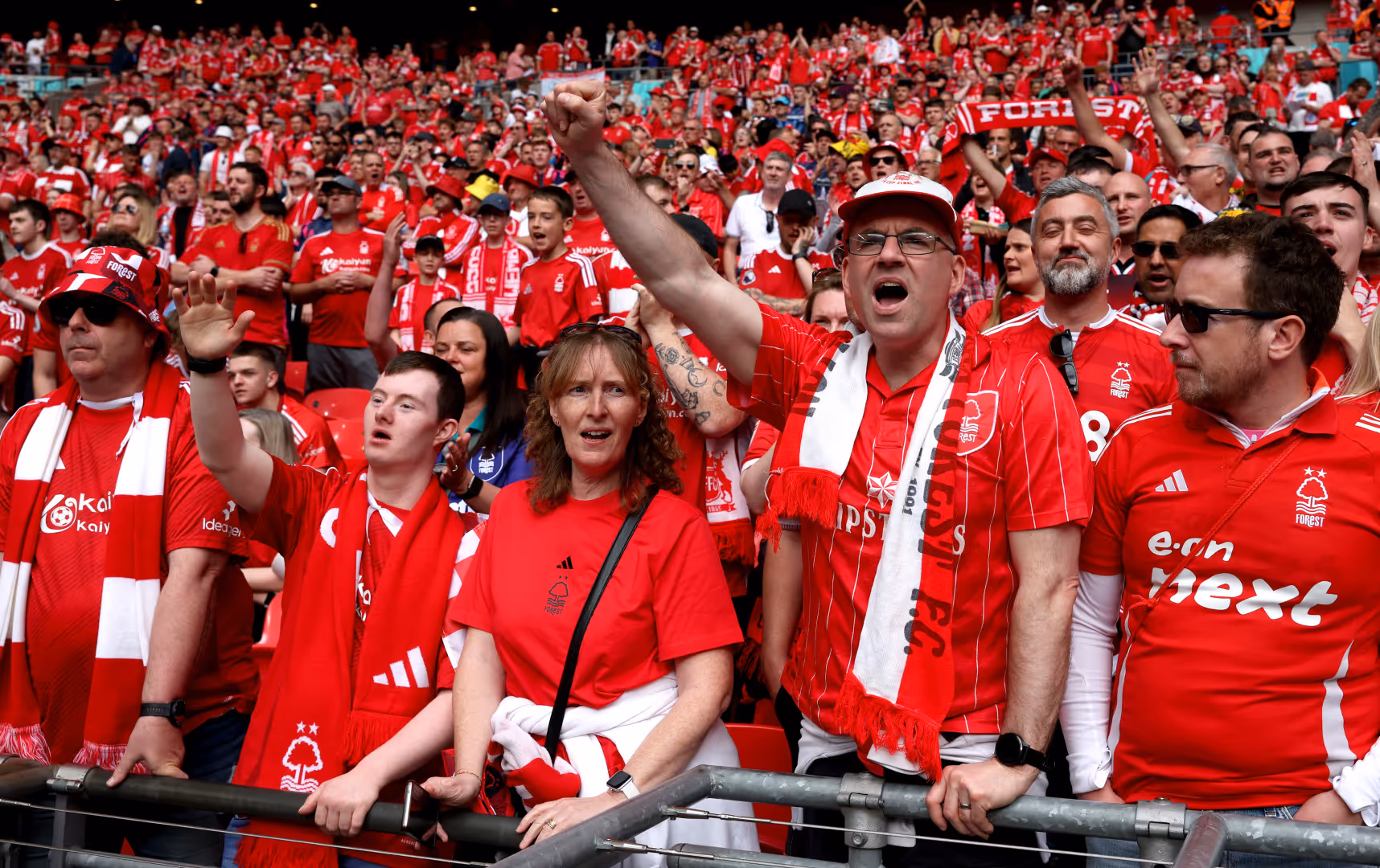 Nottingham Forest fans cheer and raise their fists while wearing club shirts.