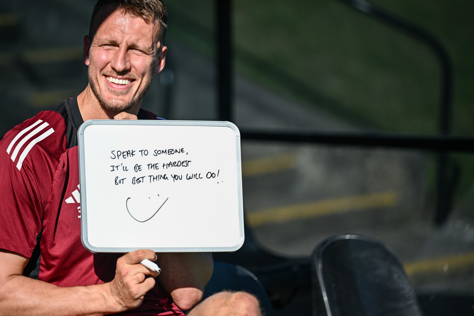 Newcastle United defender Dan Burn smiles while holding a whiteboard on which he has written: Speak to someone. It'll be the hardest but best thing you will do!