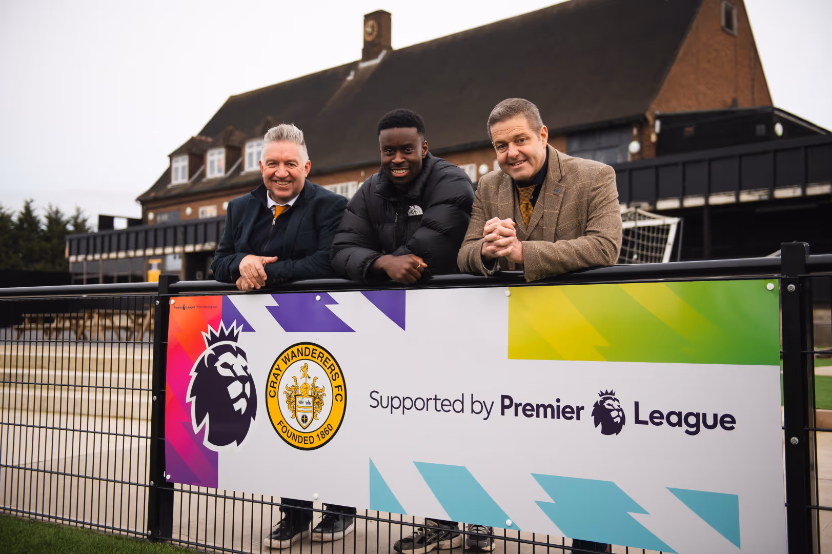 Marc Guehi poses for a photo with club representatives from Cray Wanderers, who lean on a Premier League board.