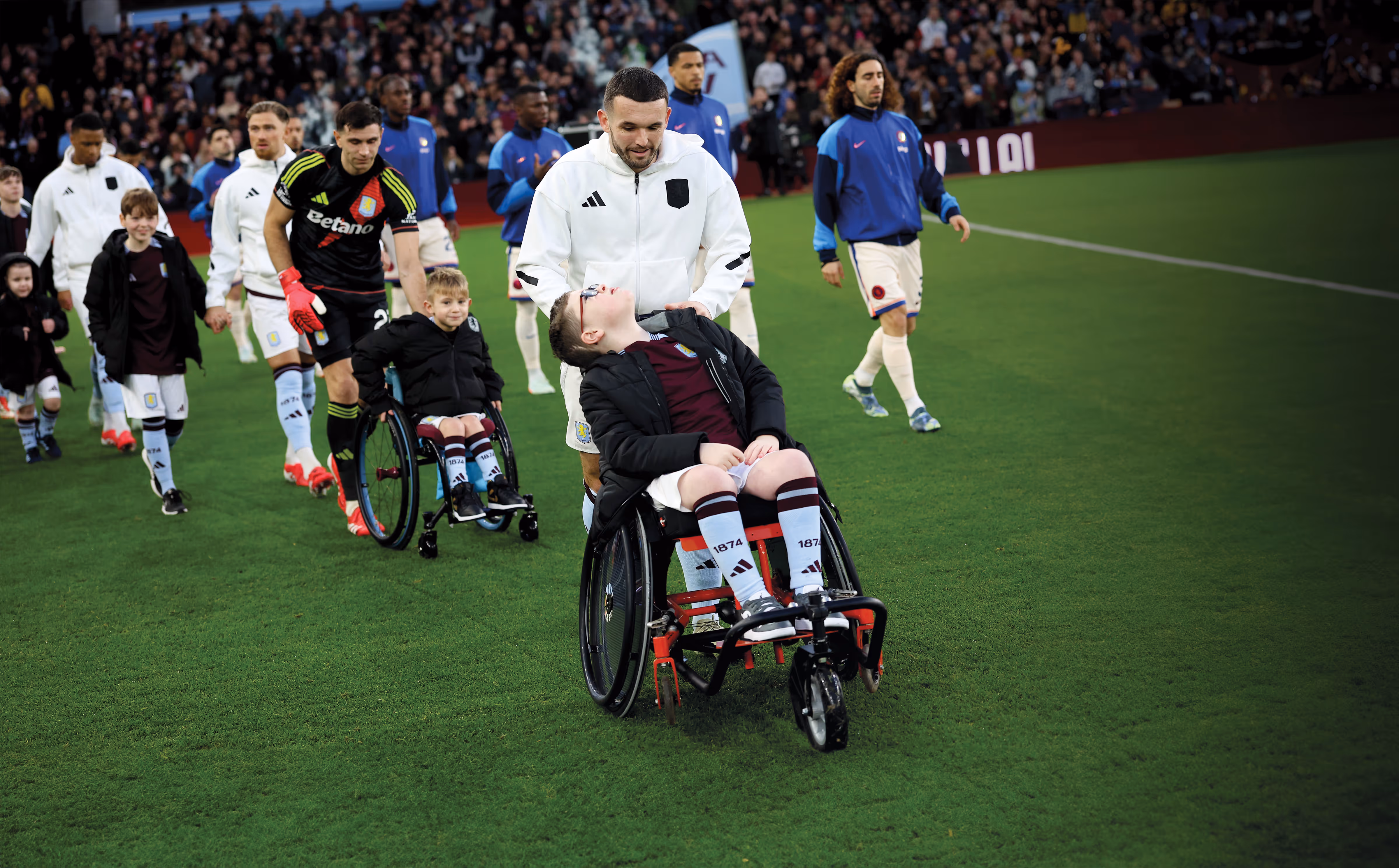 The Aston Villa team walk-out with mascots in wheelchairs ahead of their game with Chelsea. John McGinn and his mascot share a smile.