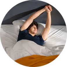 Man stretching arms while lying in bed with white sheets and orange blanket.