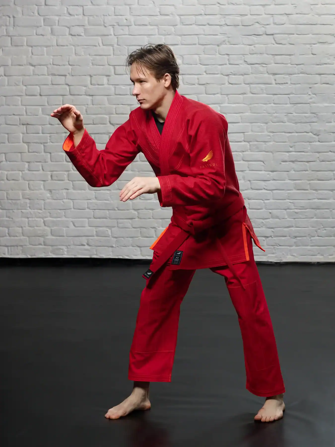 Демонстрация красного ги KAITOGI с оранжевыми акцентами: мастер в стойке для грэпплинга