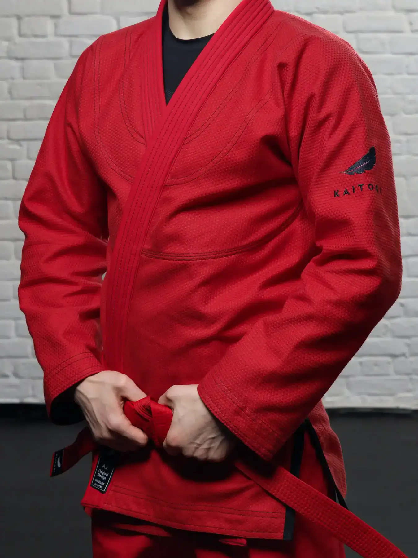 Крупный план красной куртки для грэпплинга KAITOGI: детали черной вышивки и усиленных швов вполоборота