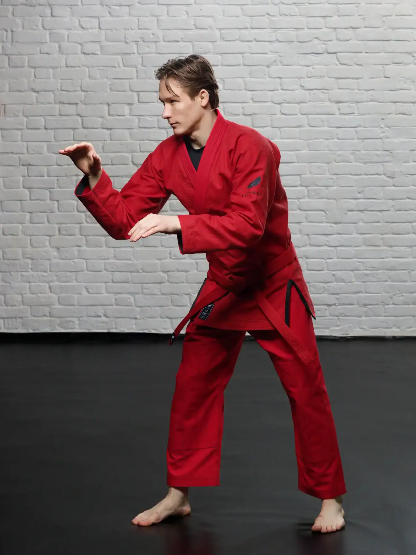 Спортсмен в боевой борцовской стойке в красном кимоно KAITOGI с черным контрастным дизайном