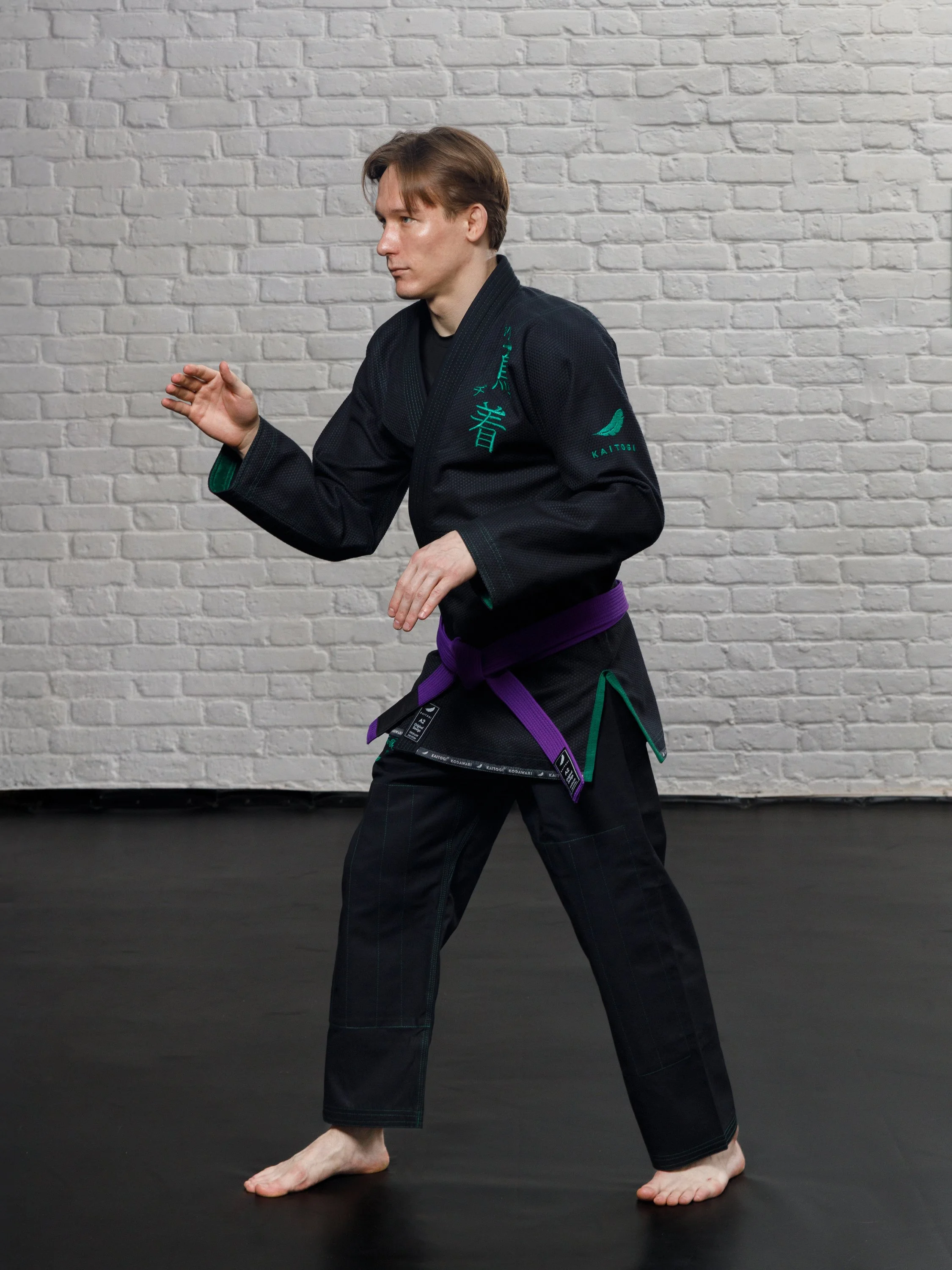 Боец в черном кимоно с зеленым дизайном в стойке для БЖЖ