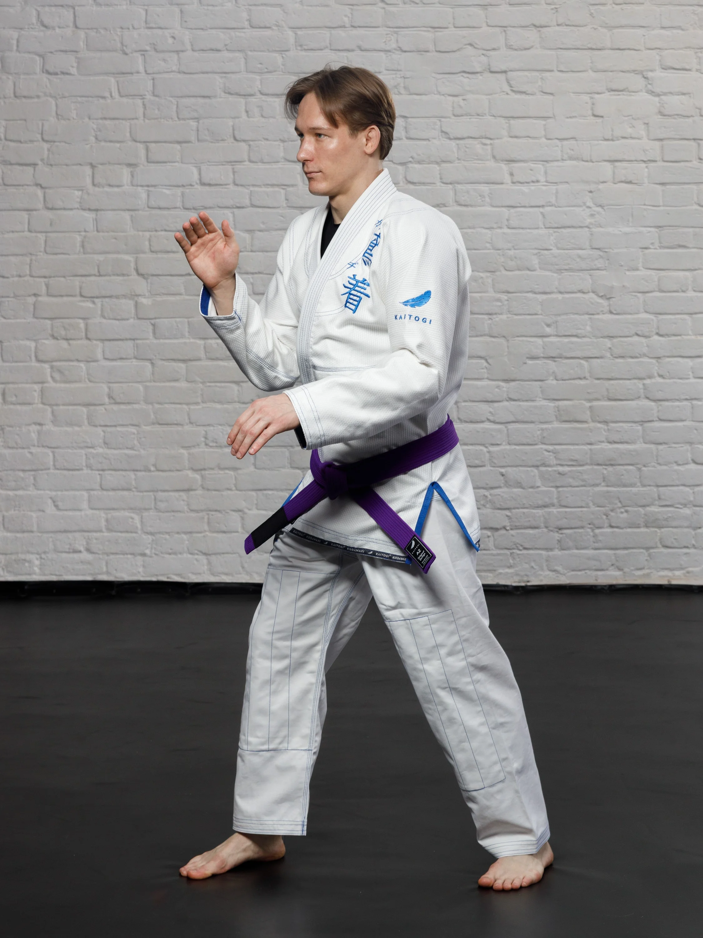 Борец в белом кимоно с синим дизайном в боевой стойке джиу-джитсу