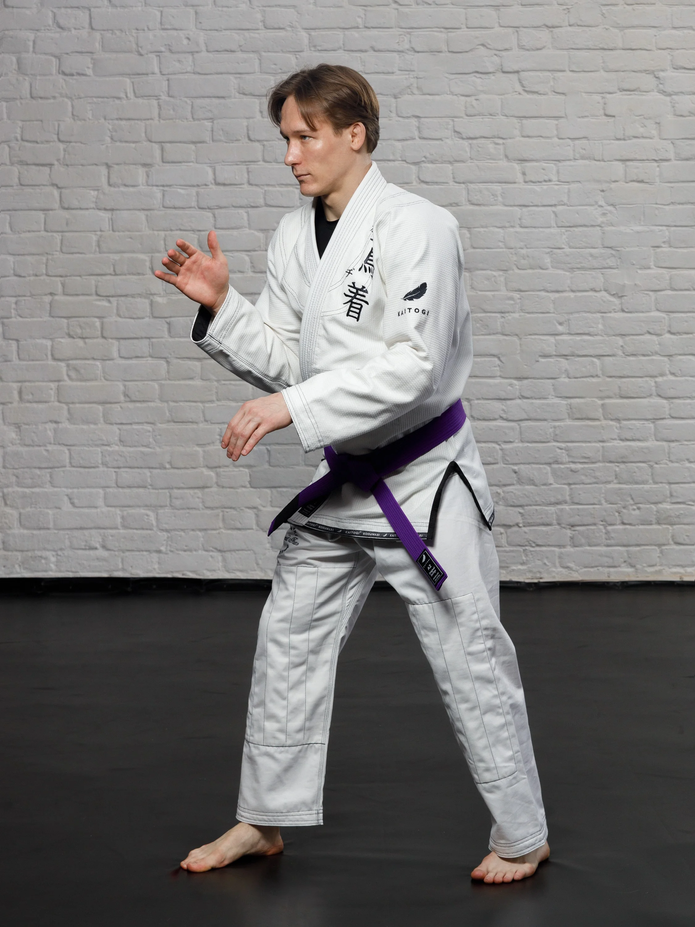 Боец в белом кимоно с черным дизайном KAITOGI в стойке