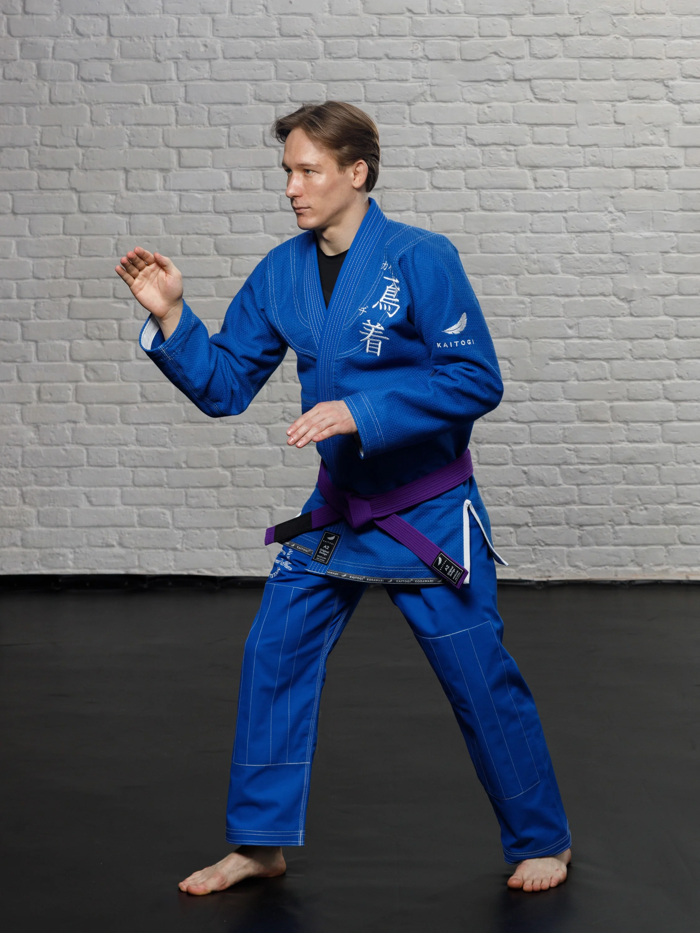 Спортсмен в синем кимоно с белым дизайном в боевой стойке джиу-джитсу