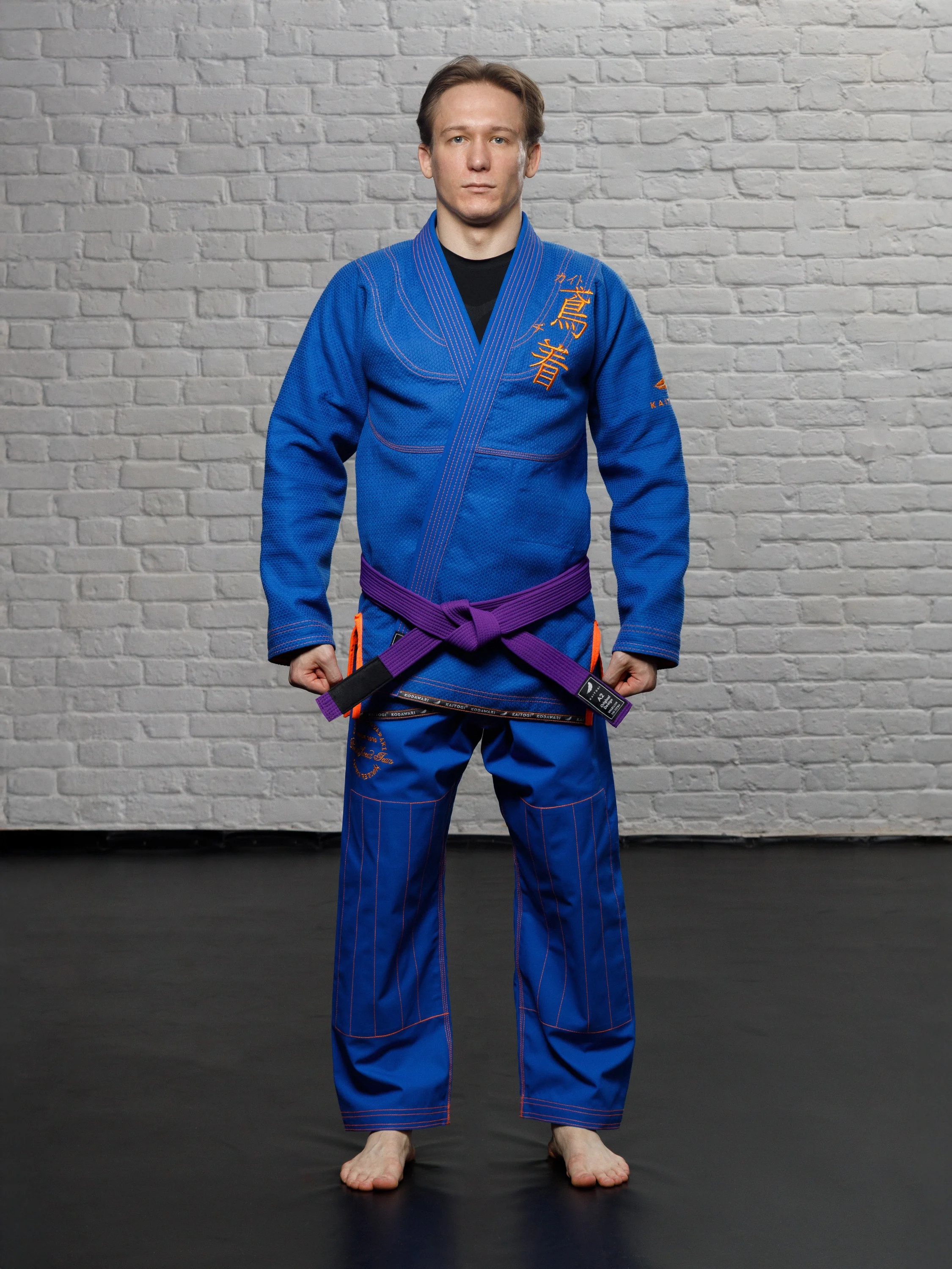 Синее ги с оранжевым дизайном на модели в полный рост, анфас. Экипировка для бразильского джиу-джитсу