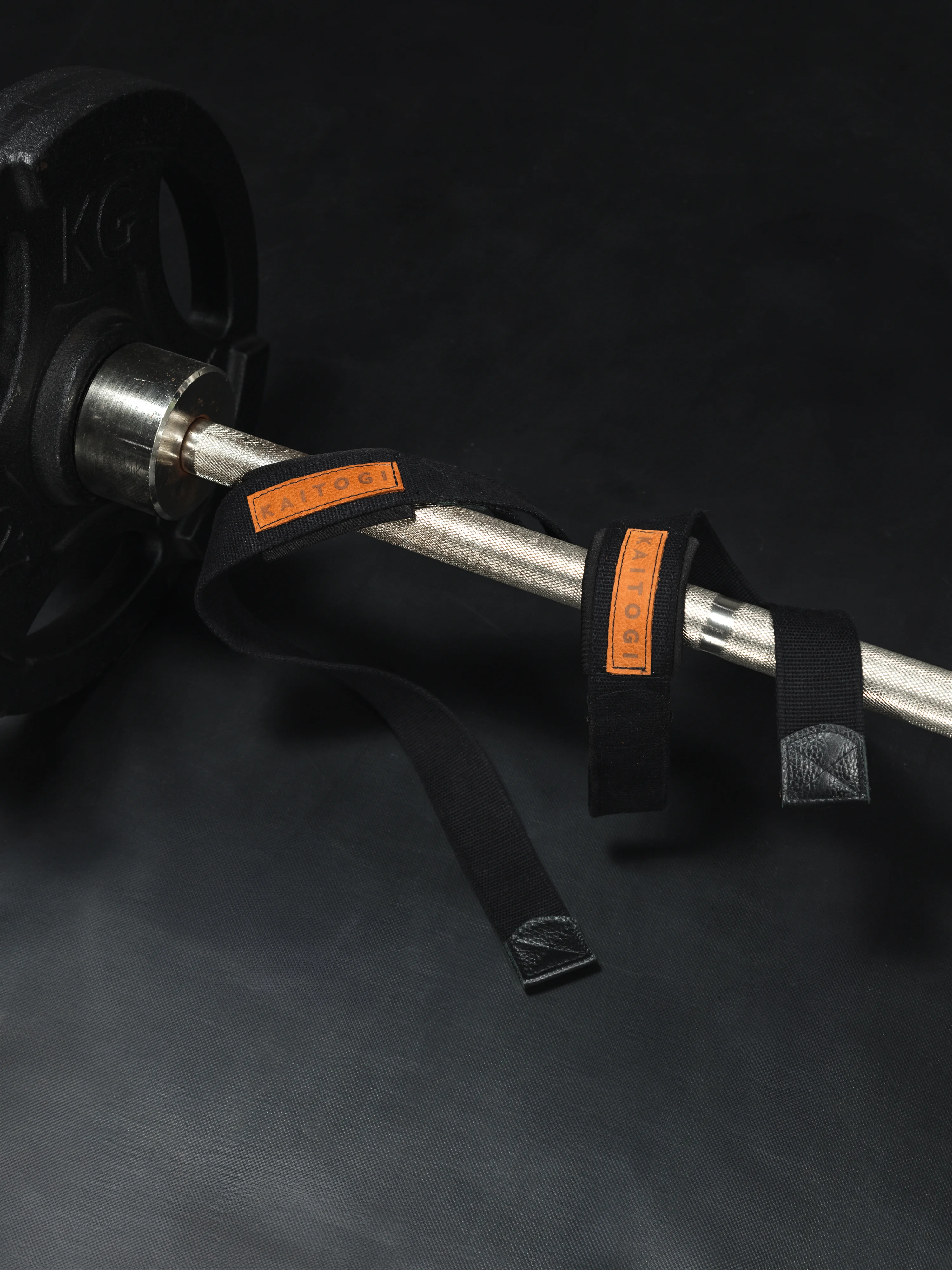 Профессиональные хлопковые лямки для тяги KAITOGI, накинутые на гриф штанги. Фото демонстрирует фактуру плотной стропы шириной 4 см и вставки из натуральной кожи с фирменным логотипом — надежный хват без повреждения кожи рук