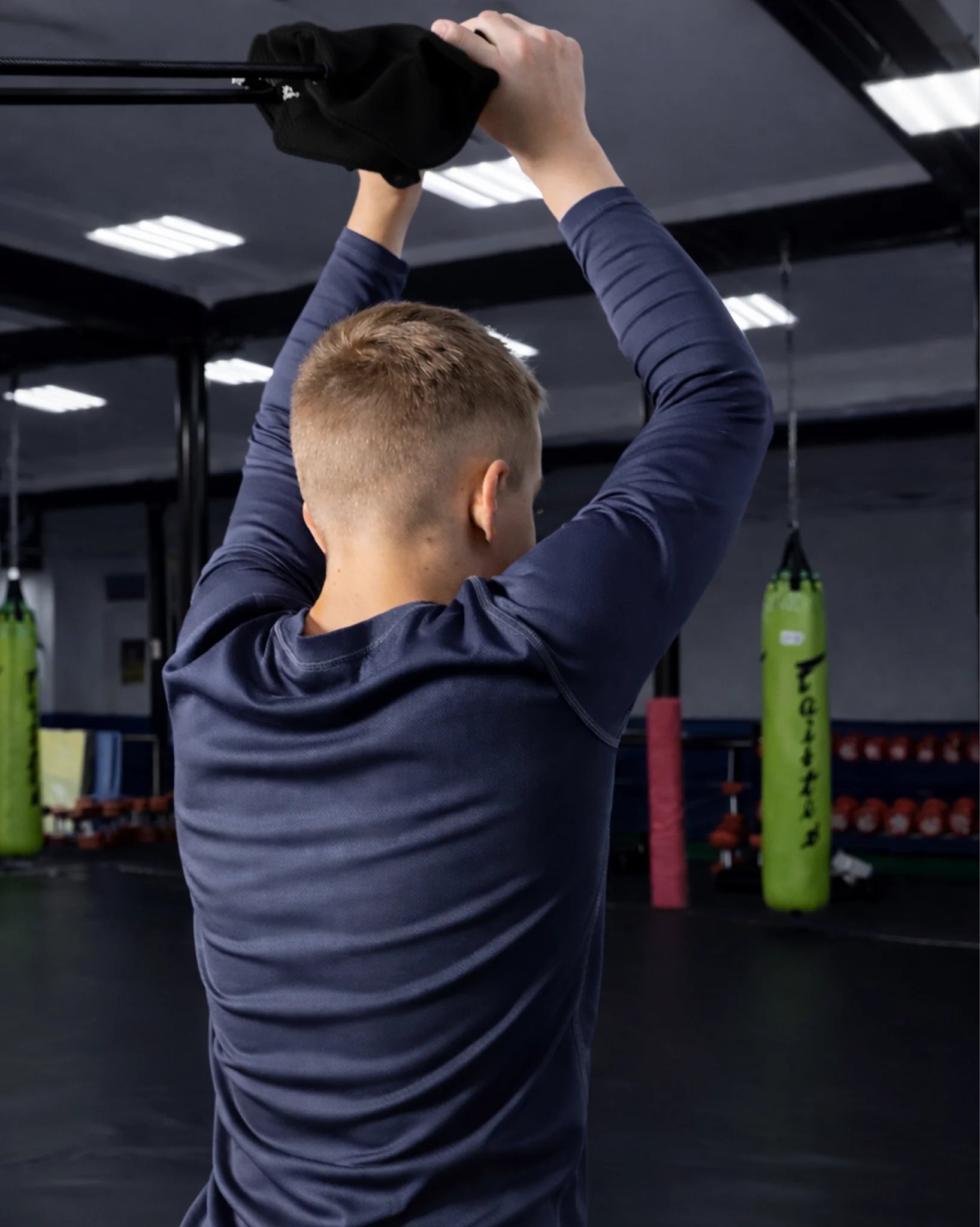 Ребенок выполняет тяговое упражнение с черной резиной Учикоми у шведской стенки