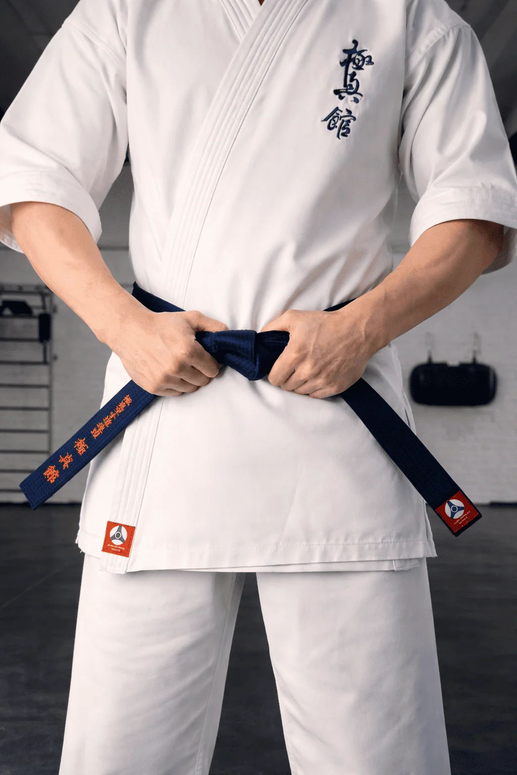 Спортсмен завязывает темно-синий пояс КАН: профессиональная экипировка для додзё