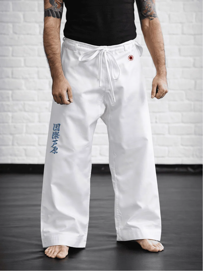 Спортсмен в белых штанах AIKO М1: традиционная длина до пола, синий иероглиф Ашихара-карате и фирменная жаккардовая этикетка