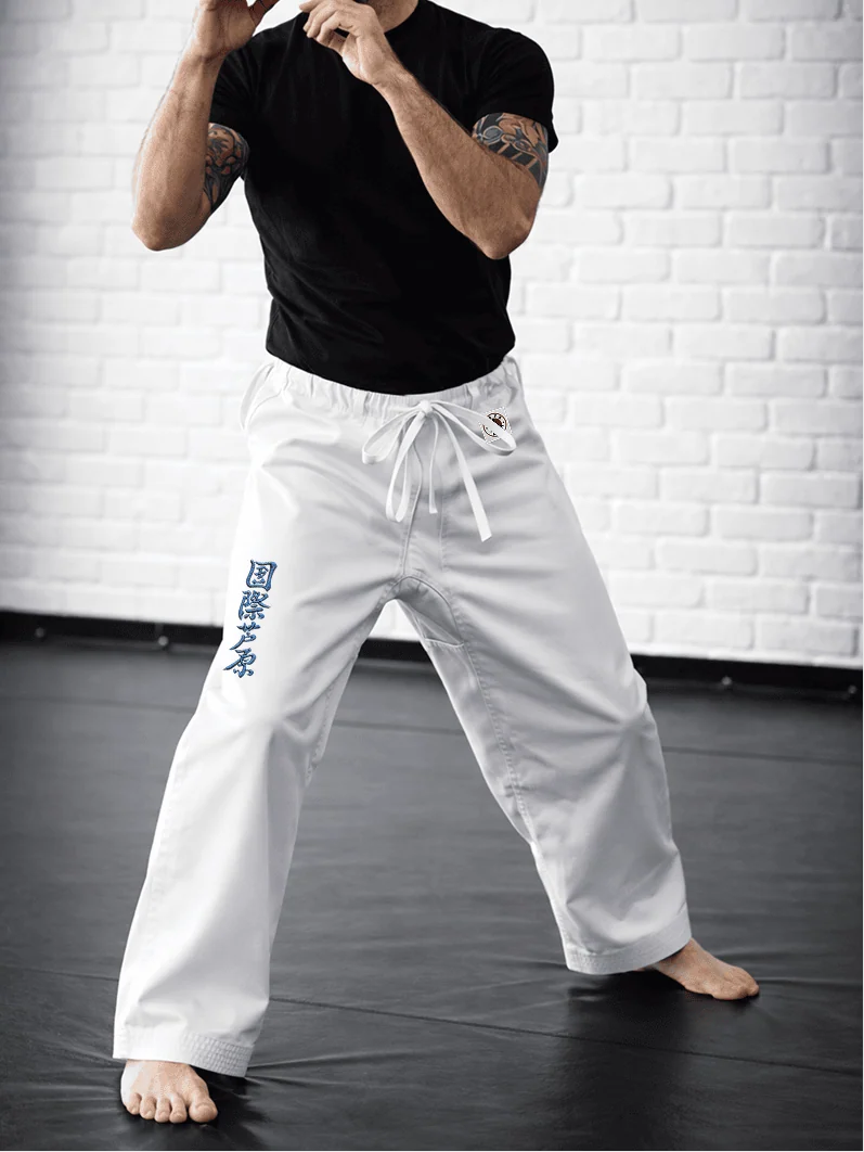 Спортсмен в белых штанах AIKO М2: укороченная длина до щиколотки, синий иероглиф Ашихара-карате и фирменная жаккардовая метка