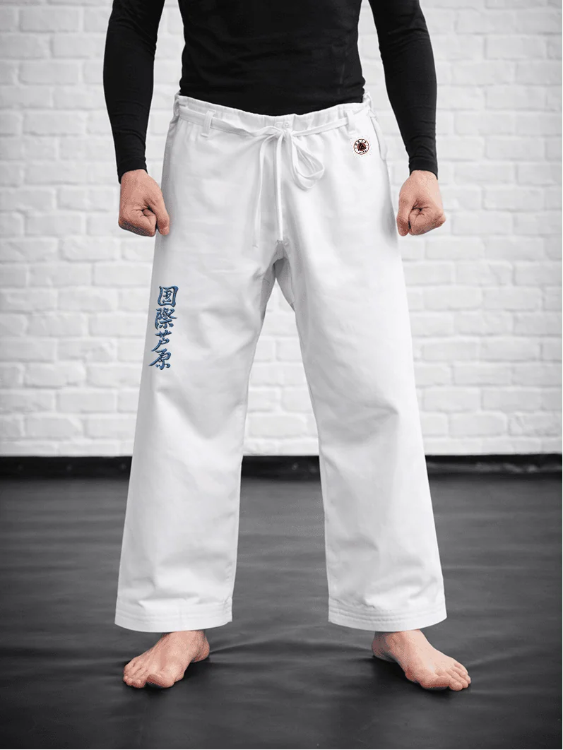 Спортсмен в белых штанах AIKO М3: укороченная длина выше щиколотки, синий иероглиф Ашихара-карате и фирменная жаккардовая метка