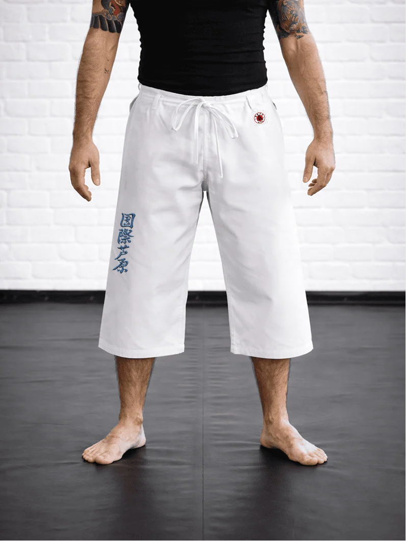 Спортсмен в белых штанах AIKO М4: укороченная длина ниже колена, синий иероглиф Ашихара-карате и фирменная жаккардовая метка