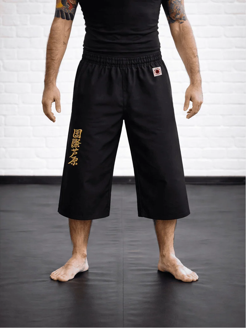 Чёрная модель AIKO М4 на спортсмене: открытая голень, золотая вышивка и фирменная жаккардовая маркировка