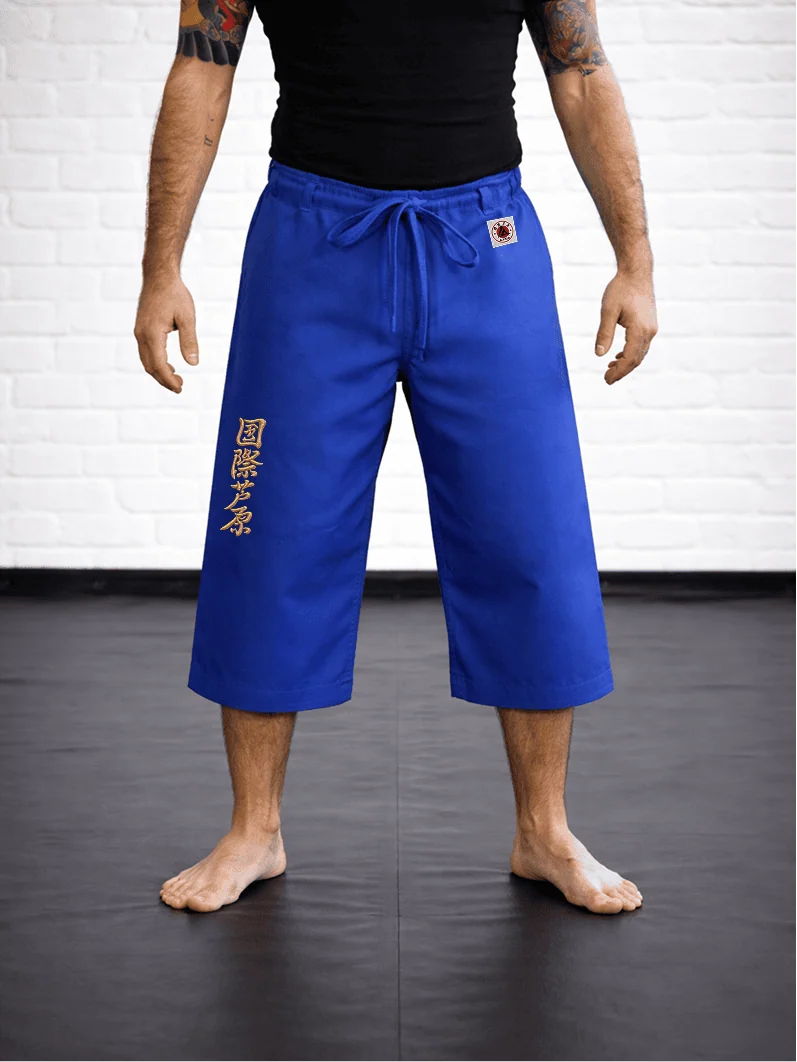 Синяя модель AIKO М4 на спортсмене: укороченный силуэт ниже колена, золотая вышивка Ашихара-карате и жаккардовый логотип