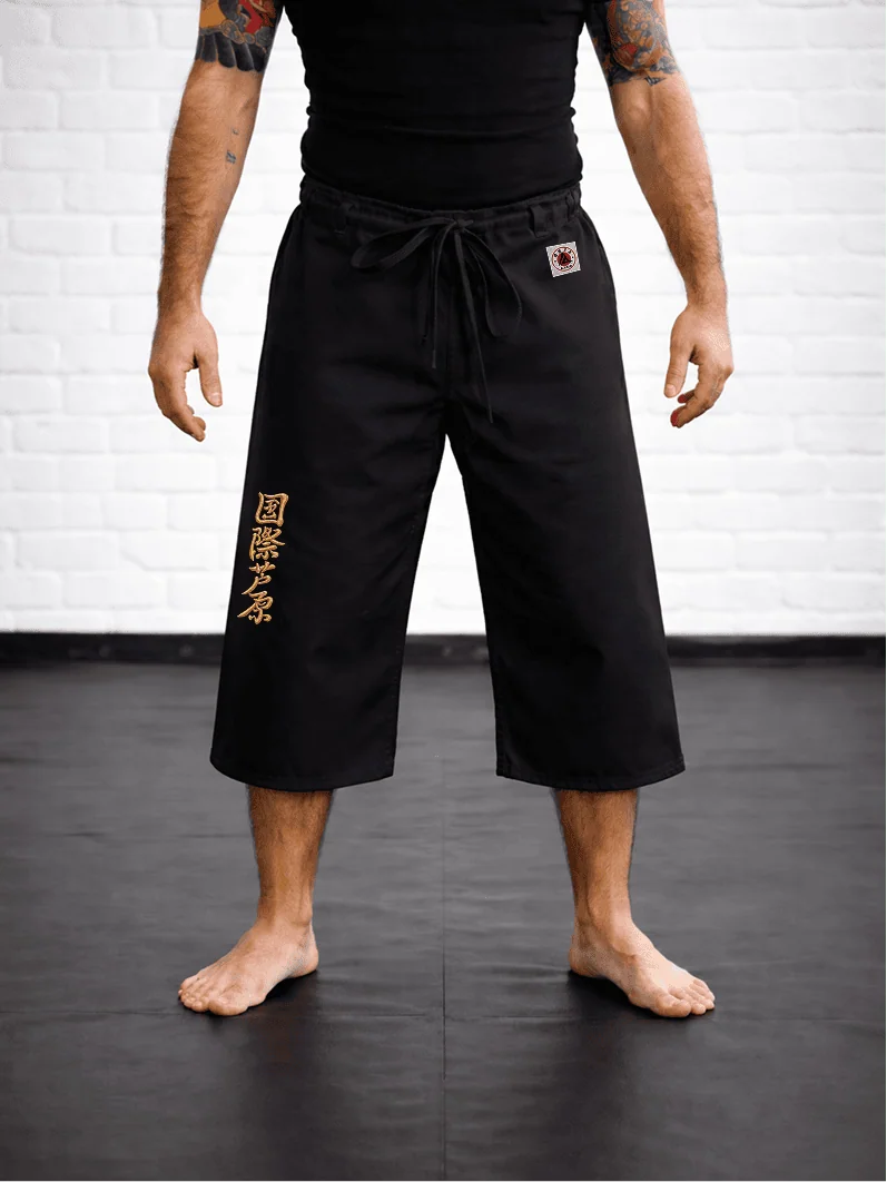 Чёрная модель AIKO М4 на резинке на спортсмене: открытая нижняя часть голени, золотая вышивка и фирменный жаккардовый знак