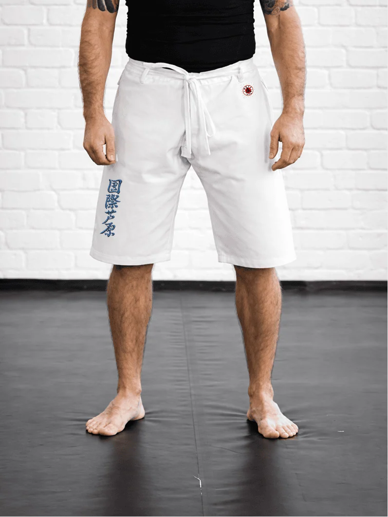 Спортсмен в белой модели AIKO М5: свободная длина выше колена, синий иероглиф Ашихара-карате и фирменная жаккардовая метка