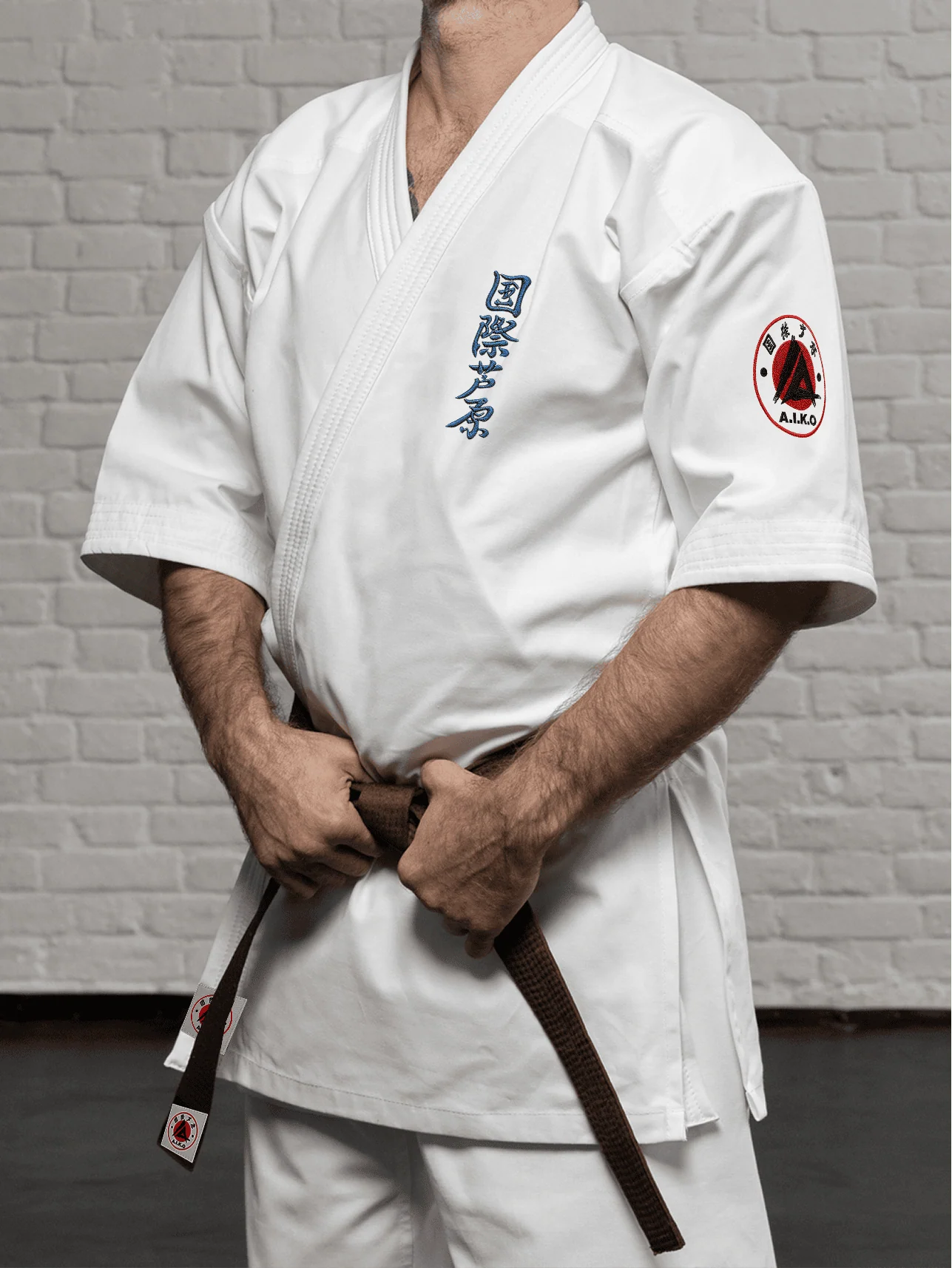 Белая куртка AIKO К2 «Наследие» на спортсмене: рукав 3/4 ниже локтя, синий кандзи Ашихара-карате и черно-красная канку A.I.K.O.