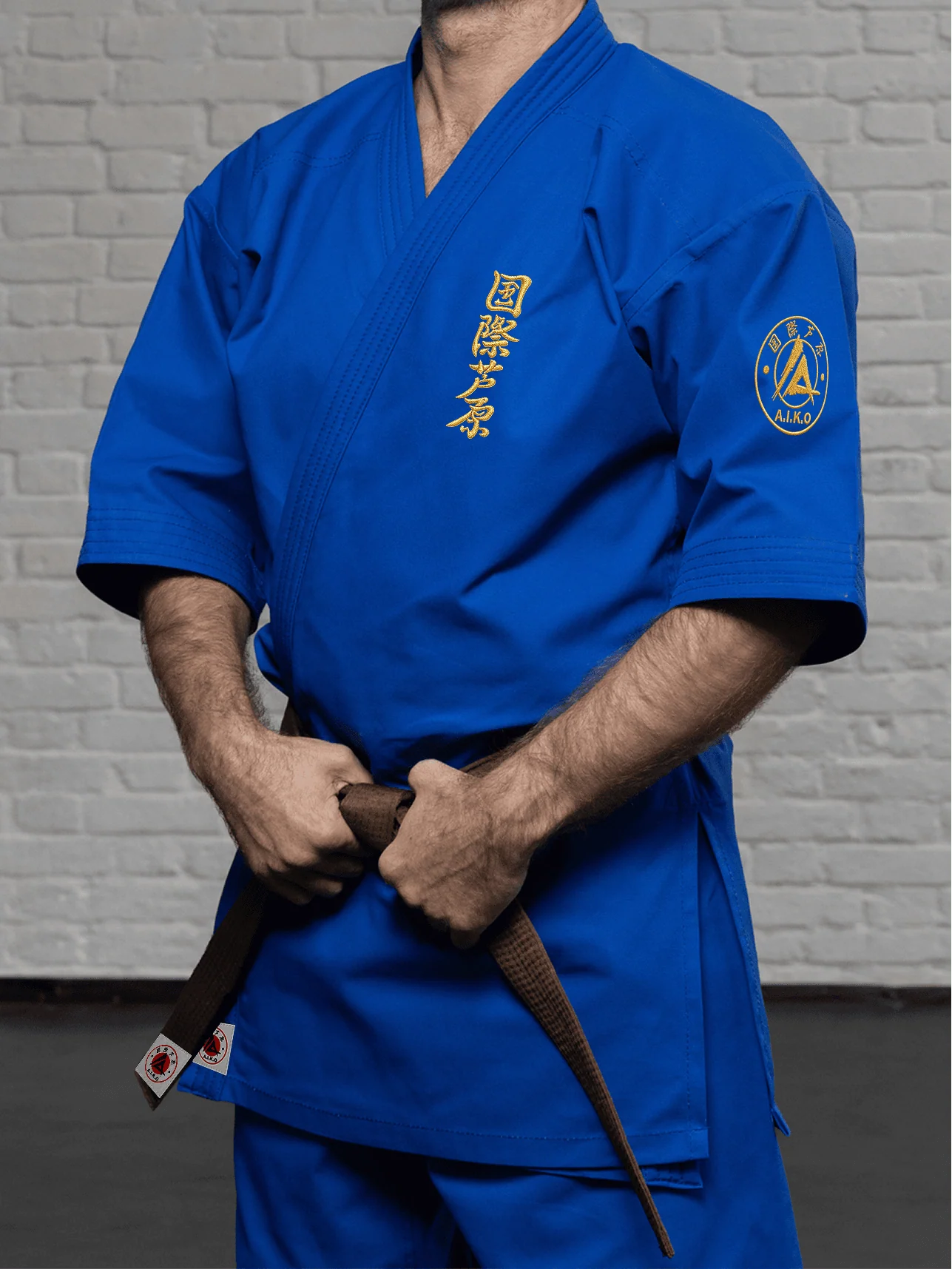 Синяя куртка AIKO К2 «Наследие» на модели: рукав 3/4 до середины предплечья, золотой кандзи Ашихара-карате и золотая канку A.I.K.O.