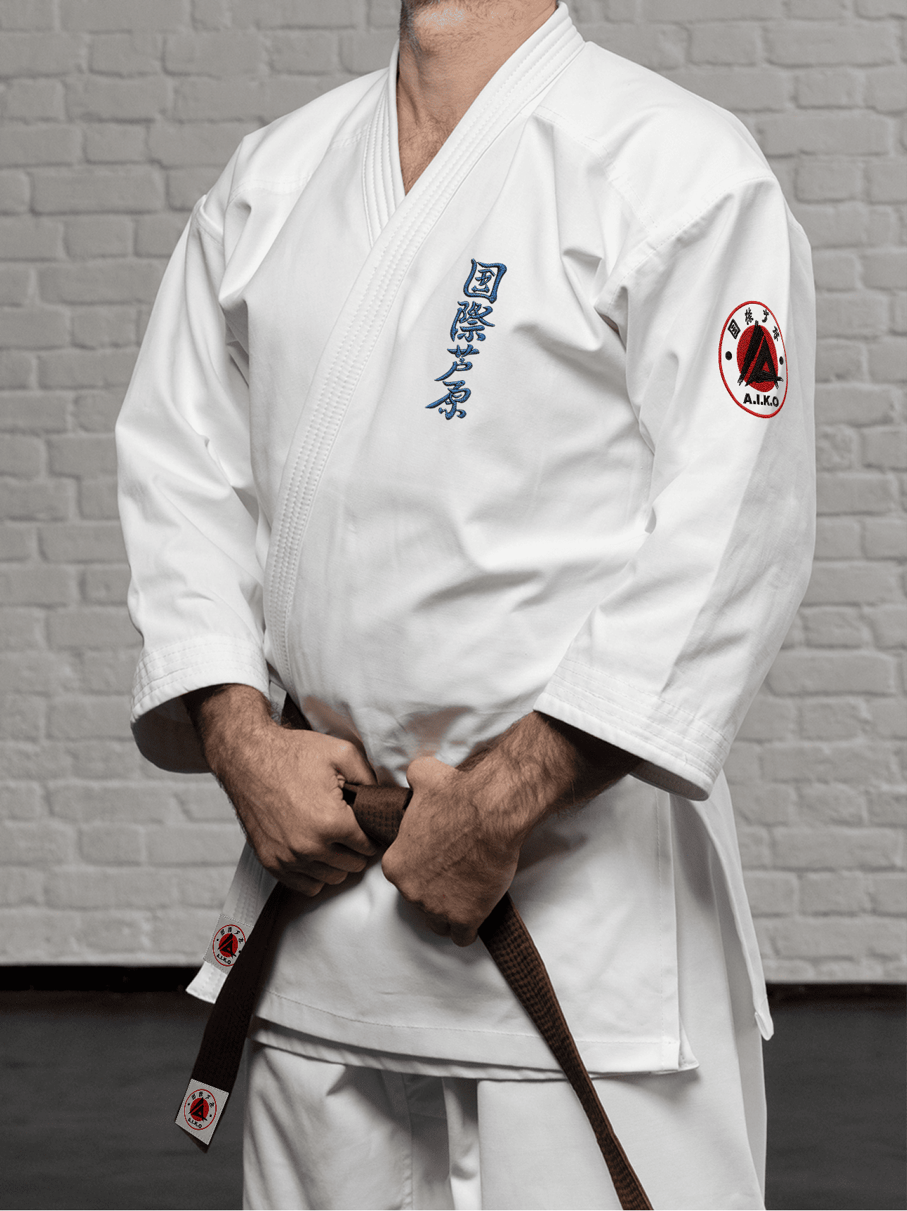 Белая куртка AIKO К3 «Наследие» на спортсмене: длинный рукав до запястья, короткий подол, синий кандзи Ашихара-карате и черно-красная канку A.I.K.O.