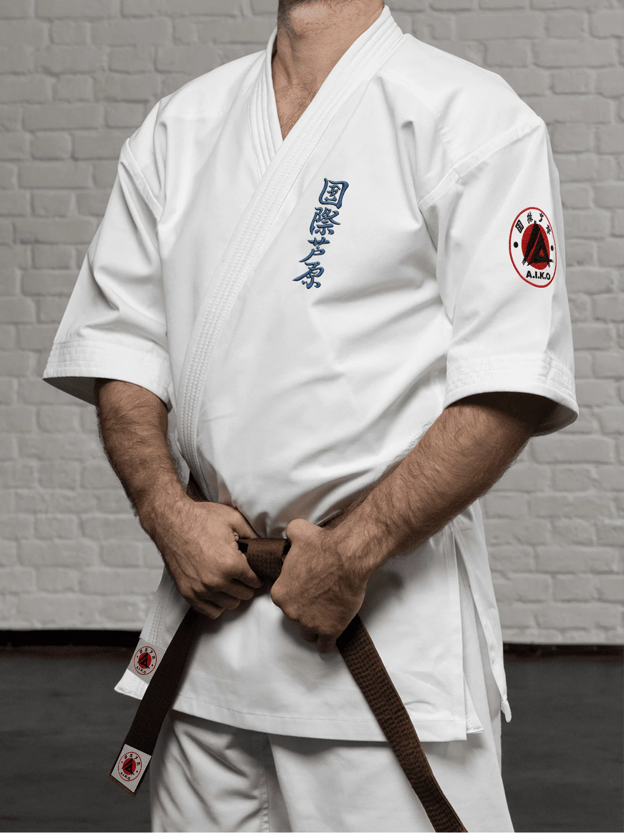 Белая куртка AIKO К4 «Наследие» на спортсмене: рукав 3/4 ниже локтя, короткий подол, синий кандзи Ашихара-карате и черно-красная канку A.I.K.O.
