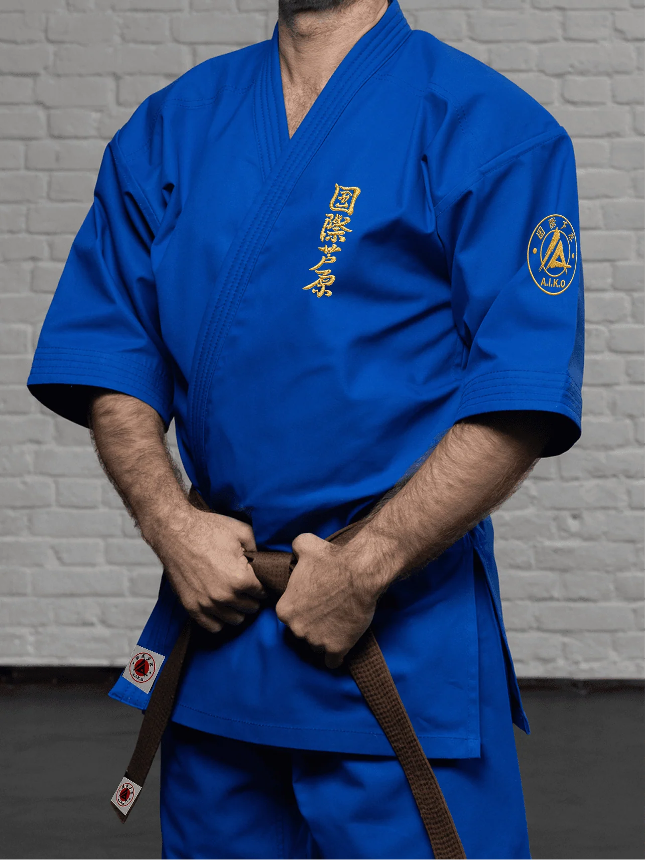 Синяя куртка AIKO К4 «Наследие» на модели: рукав 3/4 до середины предплечья, золотой кандзи Ашихара-карате и короткий подол
