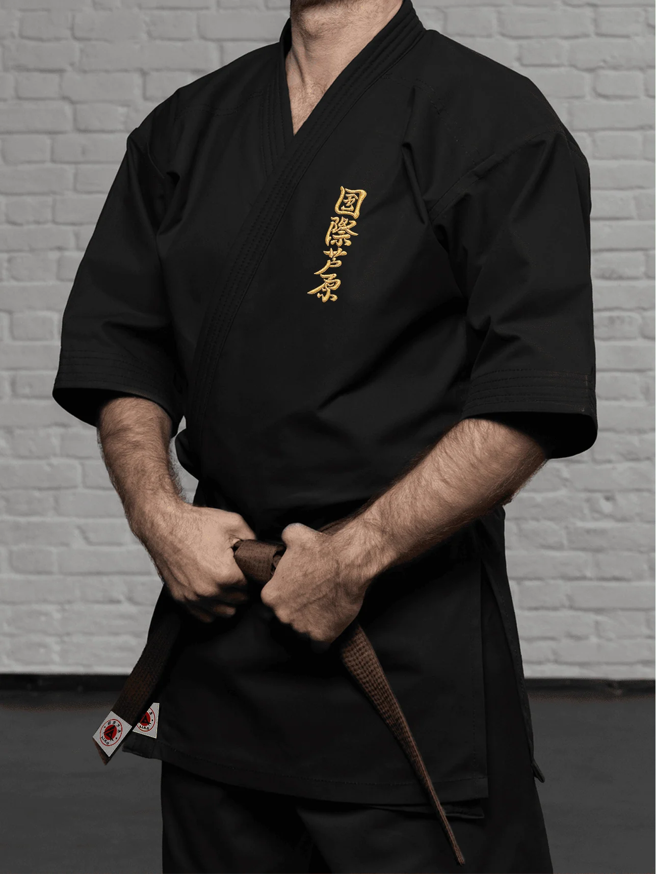 Чёрная куртка AIKO К2 «Стандарт» на спортсмене: золотой кандзи на груди, рукав ниже локтя и лаконичная классическая отделка