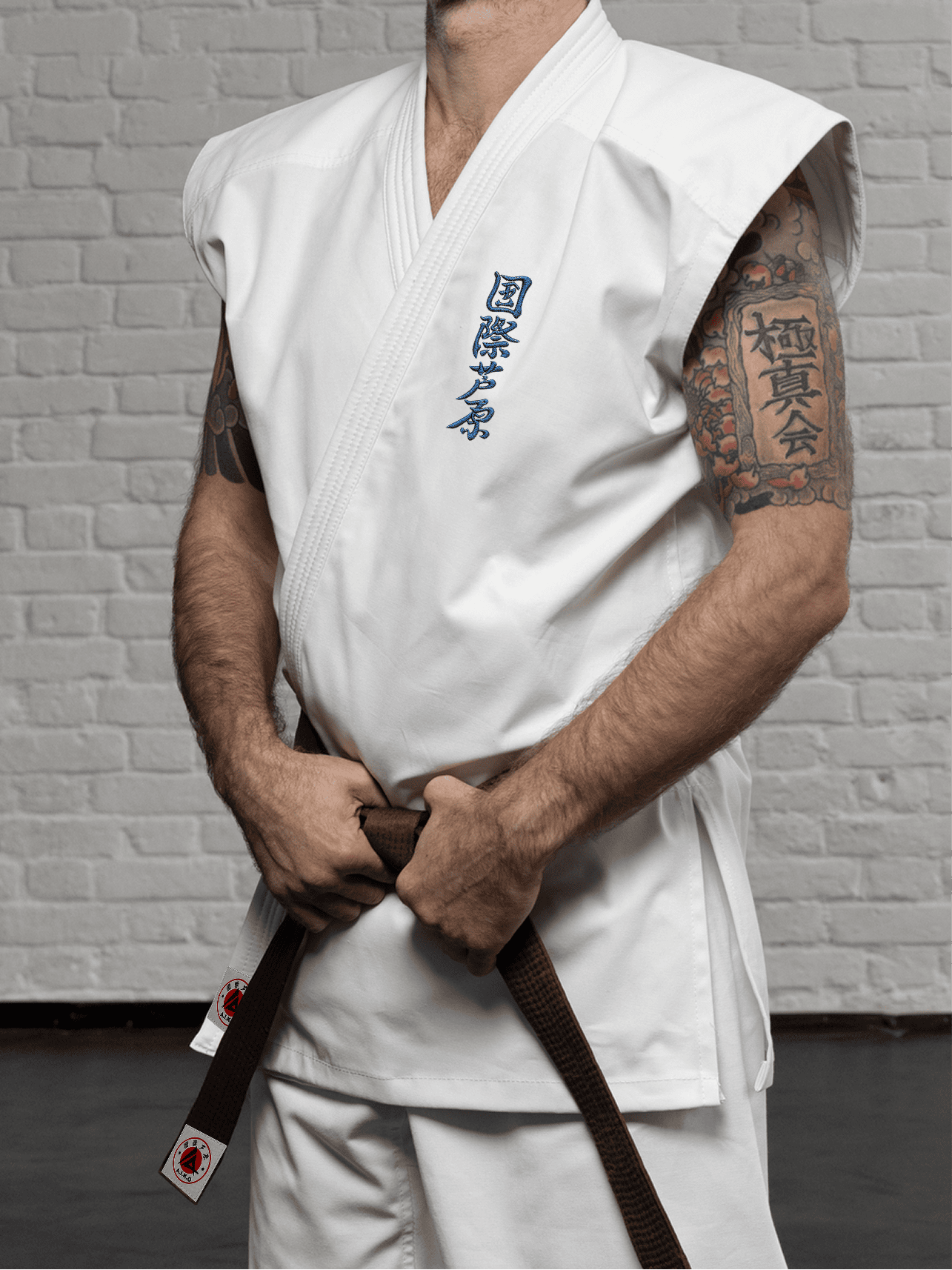 Белая куртка AIKO К6 «Стандарт» на спортсмене: модель без рукавов, синий кандзи Ашихара-карате на груди и короткий подол