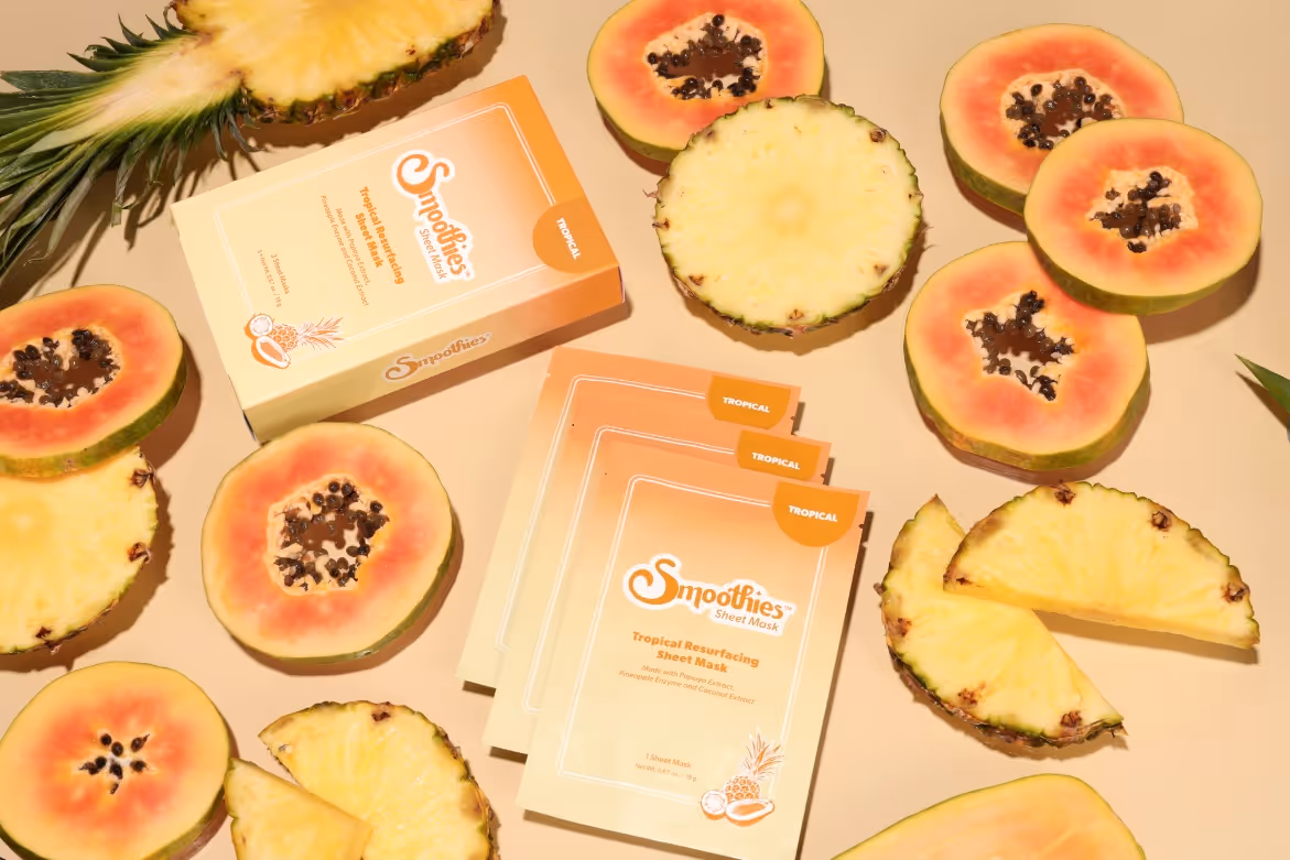Smoothies Tropical Resurfacing Sheet Masks packaging surrounded by sliced pineapple and papaya fruit.
