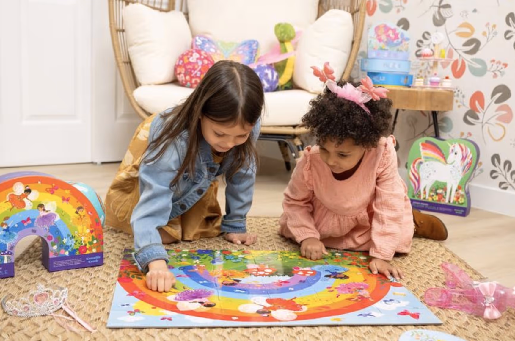 Two young girls playing a colorful fairy-themed board game on a woven rug in a cozy, decorated room.