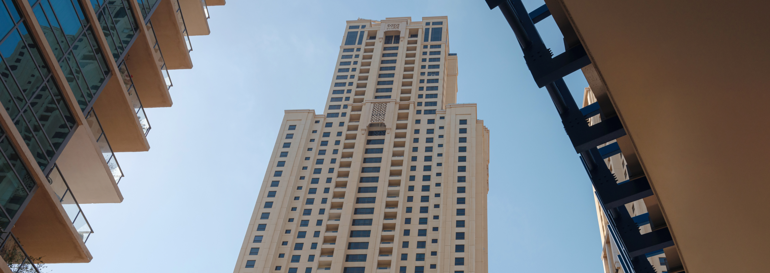 Low-angle view of a tall beige modern residential building against a clear blue sky in Dubai.