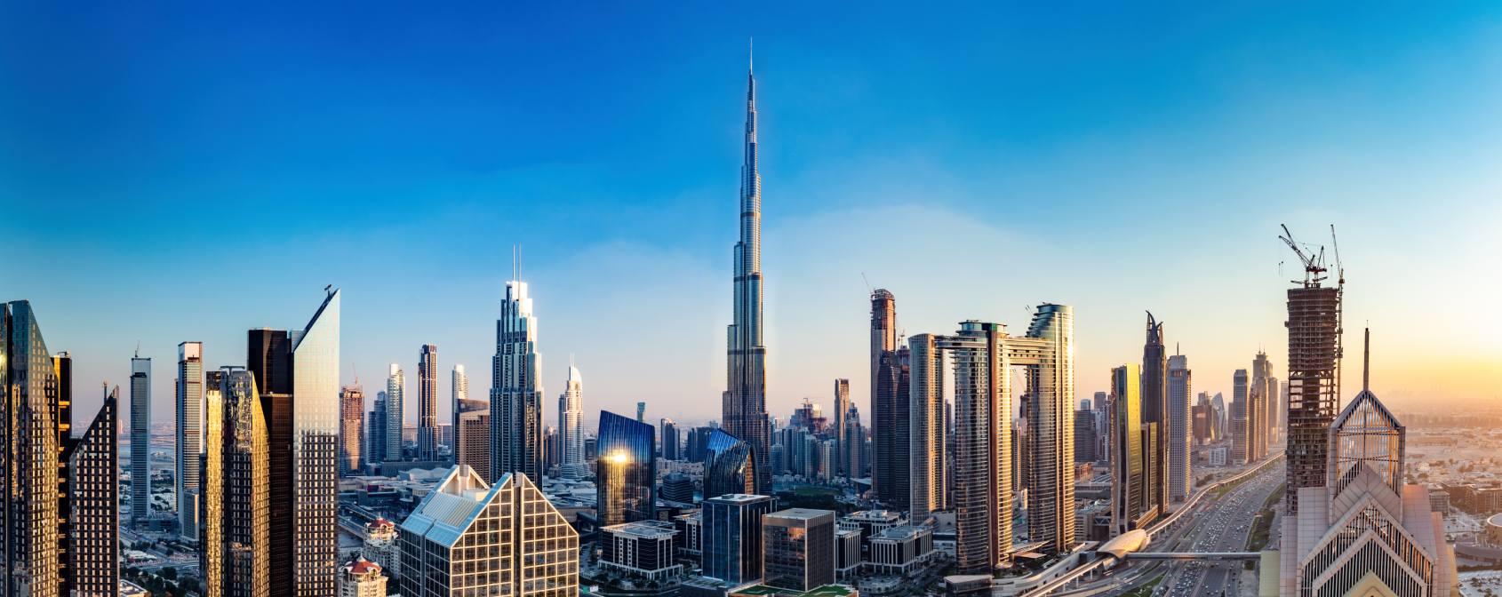 Panoramic view of Dubai skyline featuring Burj Khalifa and modern skyscrapers under a clear blue sky at sunset.