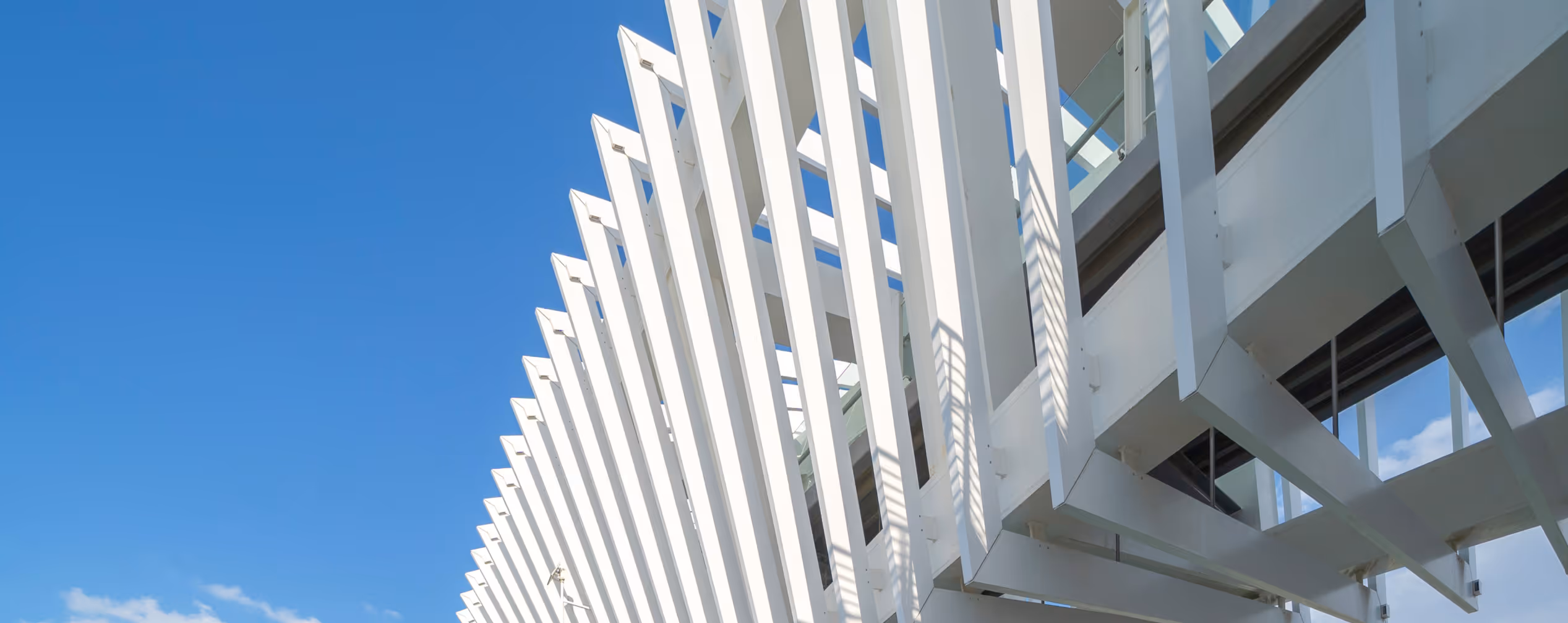 Close-up of modern white architectural beams casting shadows against a building under a clear blue sky.