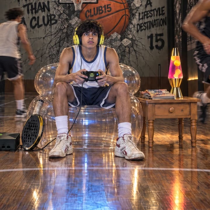 A gamer with a controller in an inflatable chair beside a lava lamp on a basketball court.
