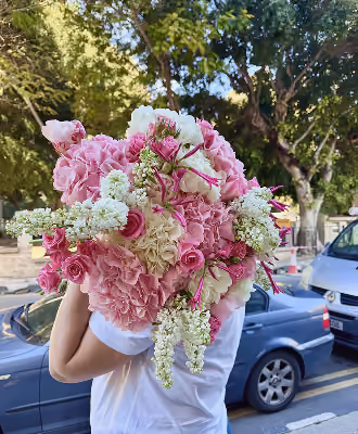 Person holding a large bouquet of pink, white, and cream flowers outdoors near parked cars.