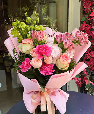 Bouquet of mixed flowers including pink roses, carnations, and green buds wrapped in pink paper.