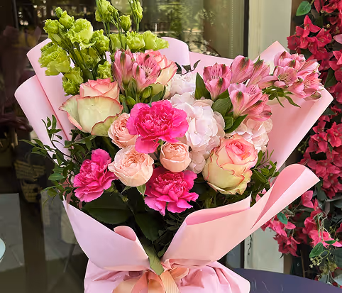 Bouquet of pink, white, and green flowers wrapped in light pink paper with a soft pink ribbon.