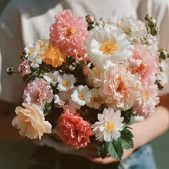 Person holding a bouquet of mixed pastel flowers including pink, white, and peach blossoms.
