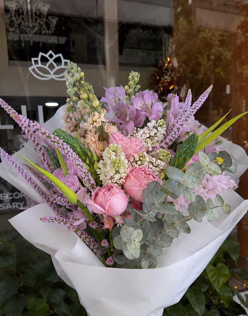 Bouquet of pink roses, white and purple flowers, and green eucalyptus leaves wrapped in white paper.