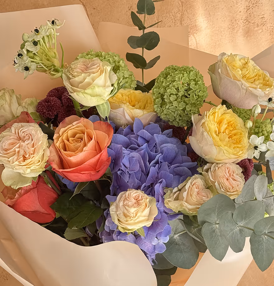 Bouquet with roses, green viburnum, purple hydrangeas, and eucalyptus leaves wrapped in cream paper.