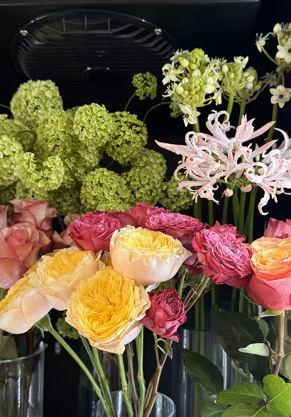 Bouquet of assorted fresh flowers including yellow roses, pink roses, green hydrangeas, and white blossoms in glass vases.