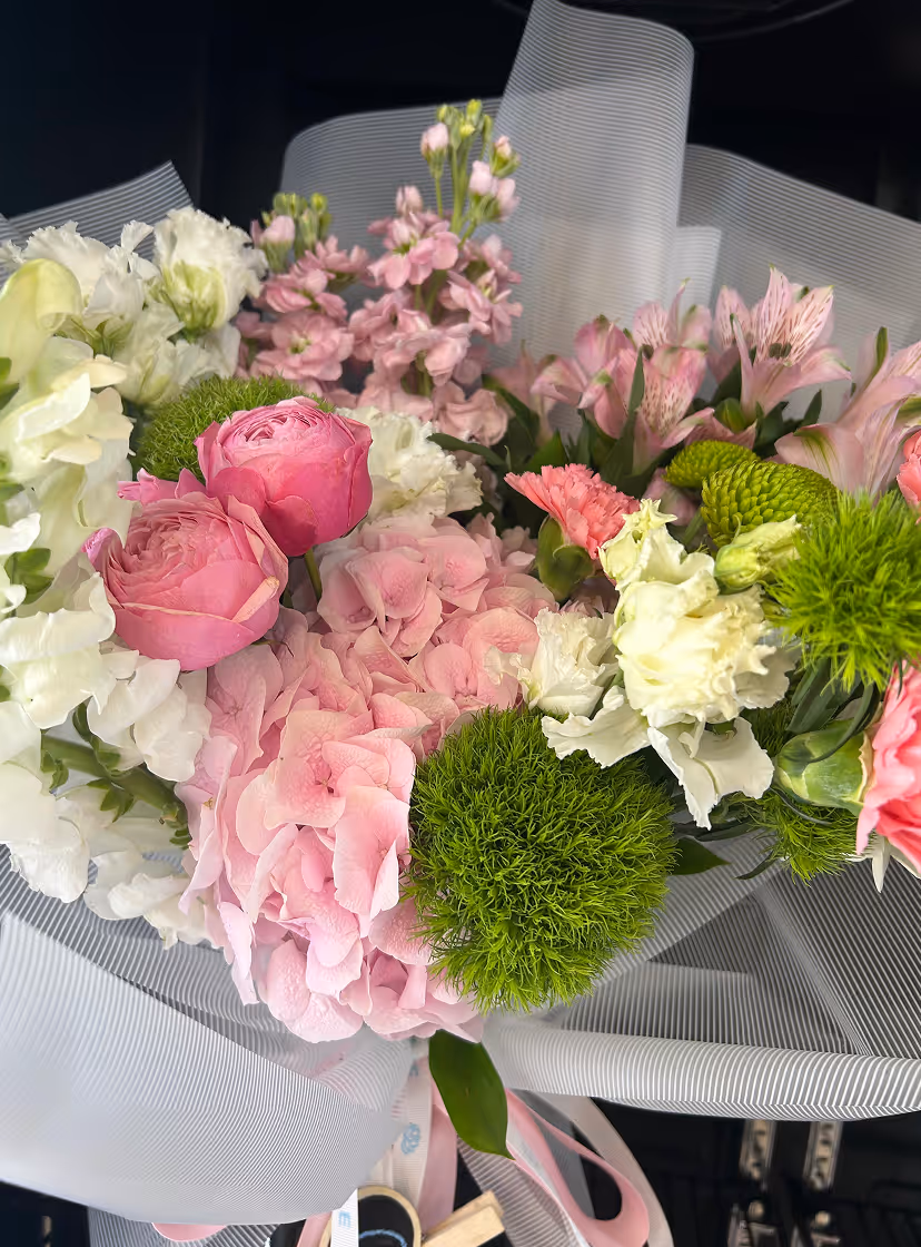 Colorful bouquet with pink roses, hydrangeas, white flowers, and green pom-pom chrysanthemums wrapped in white mesh.